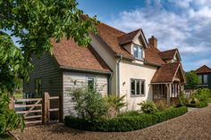 a house with a gravel driveway next to it and trees in the front yard on a sunny day