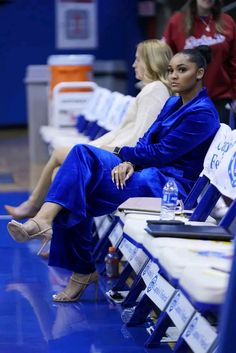 two women in blue dresses sitting next to each other at a basketball game on the court