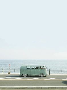 an old vw bus driving down the road by the ocean