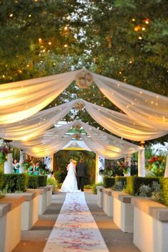 a bride and groom are walking down the aisle at their wedding ceremony with white drapes draped over them