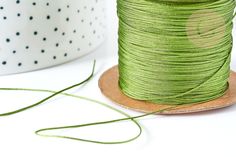 a spool of green thread sitting on top of a wooden plate next to a white bowl