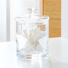 a glass jar filled with white cotton swabs sitting on top of a table