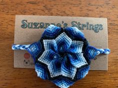 a crocheted blue and white flower on a wooden table with a business card