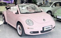 a pink convertible car is on display in a showroom with other cars behind it