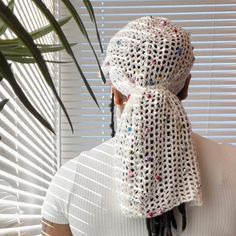 a woman wearing a white scarf with multicolored beads is looking out the window