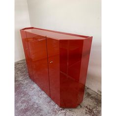 a red cabinet sitting in the corner of a room with concrete flooring and white walls