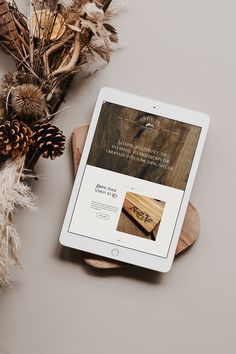 an ipad sitting on top of a wooden table next to some dried plants and pine cones