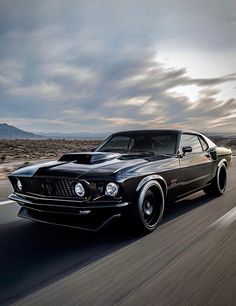 a black car driving down the road with clouds in the background