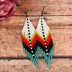 two pairs of beaded earrings on top of a wooden table next to pink flowers