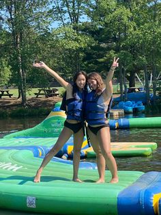 two girls are standing on inflatable rafts at the lake