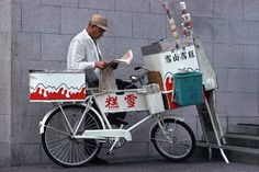 a man sitting on top of a white bike next to a gray wall with writing on it