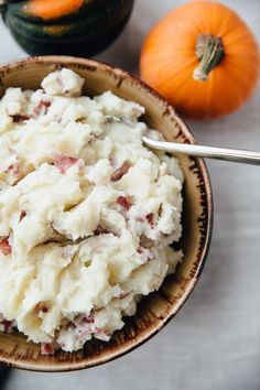 mashed potatoes with bacon in a bowl next to two pumpkins on the table