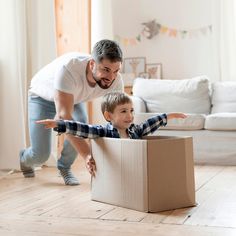 a father and son playing with a cardboard box on the floor in their living room