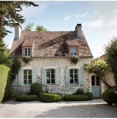 a stone house with blue shutters and trimmed hedges