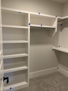 an empty walk in closet with white shelving and blue tape on the shelves for storage