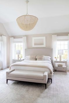 a large white bed sitting in a bedroom next to two windows and a chandelier