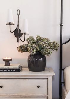 a black vase with flowers sitting on top of a white dresser next to a lamp