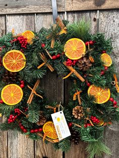 a christmas wreath with oranges and pine cones hanging on a wooden fence next to a tag