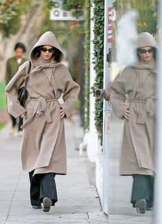 a woman is walking down the sidewalk wearing a coat