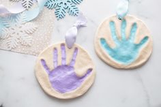 two handprinted ornaments on a table with snowflakes