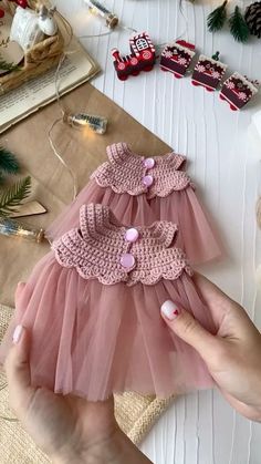 a hand holding a pink dress on top of a table next to christmas decorations and other items