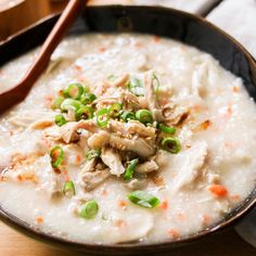 a bowl filled with rice and meat on top of a wooden table next to a spoon