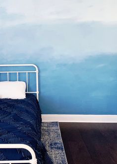 a bed in a room with blue walls and wooden floors, along with a rug on the floor