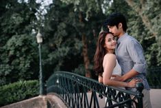 a man and woman standing next to each other on a bridge in front of trees