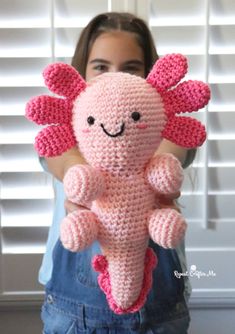 a woman holding up a pink crocheted stuffed animal