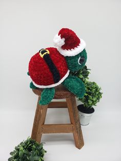 a stuffed turtle wearing a santa hat sitting on top of a wooden stool next to a potted plant