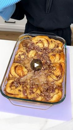 a person in blue gloves holding up a pan filled with cinnamon bundts on top of a table