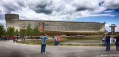 people standing in front of a large building with a giant boat on it's side