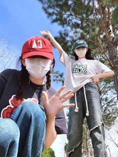 two children wearing face masks while standing next to each other in front of a tree