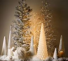 an assortment of christmas trees and candles on a mantle in front of a grey background