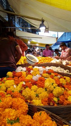 people shopping at an open air market with baskets full of flowers on the ground and in front of them