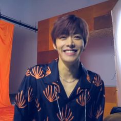 a person standing in front of an orange curtain and wearing a black shirt with flowers on it