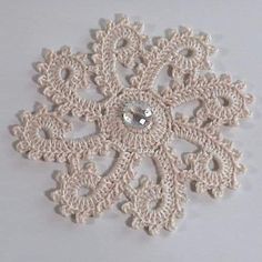 a crocheted snowflake is shown on a white tablecloth with a small diamond in the center