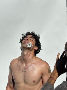 a man with no shirt on eating something off of his face while standing next to a pole