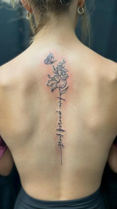 the back of a woman's upper back tattoo with flowers and words on it