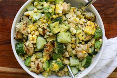 a white bowl filled with corn and cucumbers on top of a wooden table