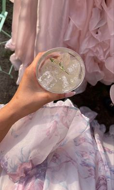 a person holding a drink in front of some pink dress material on the ground,