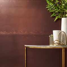 a table with two vases on it next to a brown wall and a plant