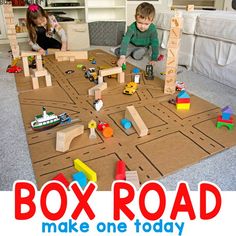 two children playing with toys on the floor in a living room next to a cardboard box road