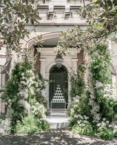 an entrance to a building with white flowers and greenery on the outside, surrounded by trees