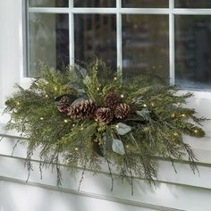 a wreath with pine cones and greenery hanging on a window sill in front of a house