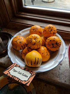 some oranges with faces drawn on them are sitting on a plate near a window