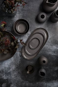 the table is set with gray dishes and vases on it, including one bowl