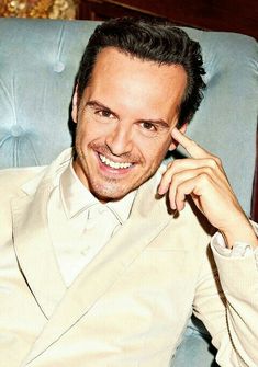 a man sitting in a blue chair with his hand on his head and smiling at the camera