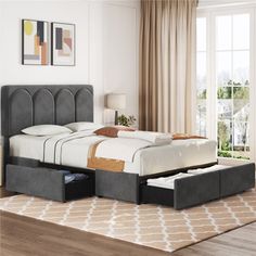 a bed with two drawers underneath it in a living room next to a large window