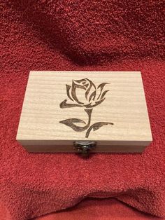 a wooden box sitting on top of a red towel covered in a rose design with black ink